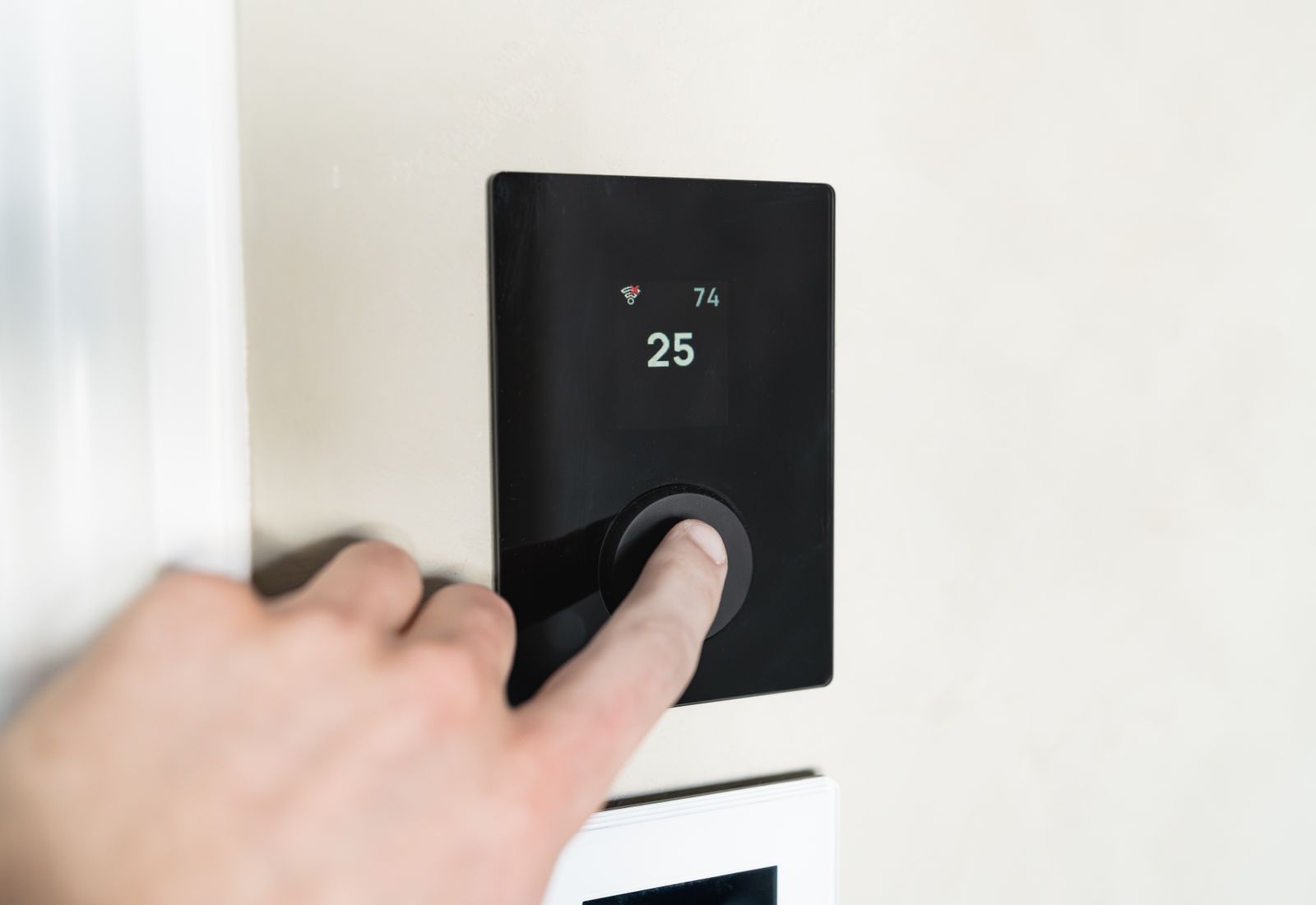 A hand adjusting a modern wall thermostat